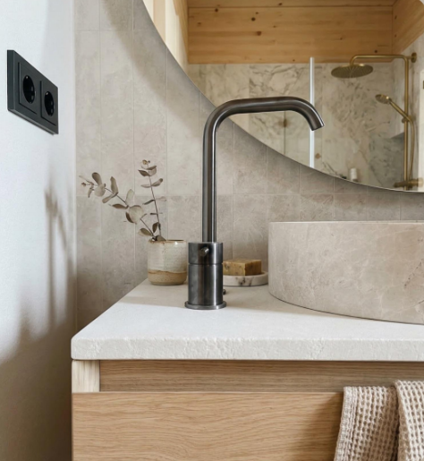 Lavabo mecanizado en encimera de Limepearl sobre mueble de madera, con grifería negra.
